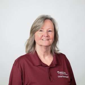 smiling woman with gray hair maroon shirt blank background