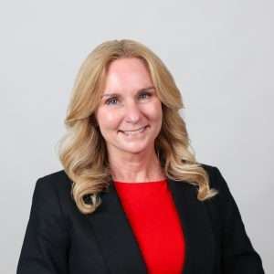woman in black blazer with red shirt smiling in front of blank background