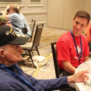 male student listening to a military veteran at a table while drinking coffee
