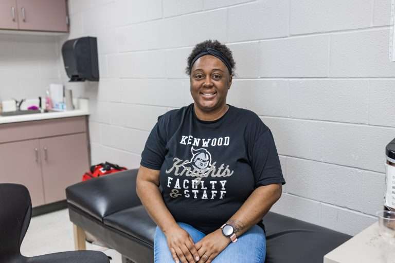 high school nurse wearing black tshirt and black headband sitting on nurses table