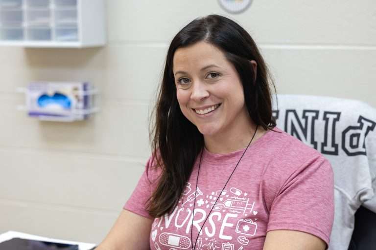 school nurse wearing pink tshirt smiling in her office