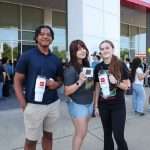 three students show promotional items in front of car dealership