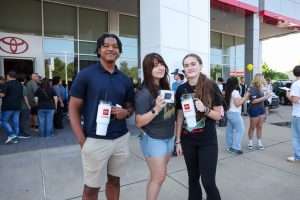three students show promotional items in front of car dealership