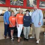 five people standing in car dealership showroom smiling