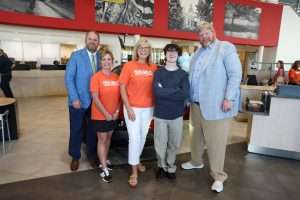 five people standing in car dealership showroom smiling