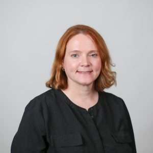 woman in black shirt with red hair smiling in front of blank background