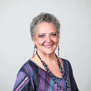 woman in colorful shirt necklace and earrings smiling in front of blank background