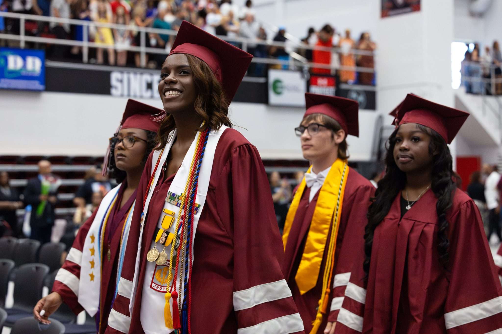 group of four graduates walking into room wearing maroon gowns smiling