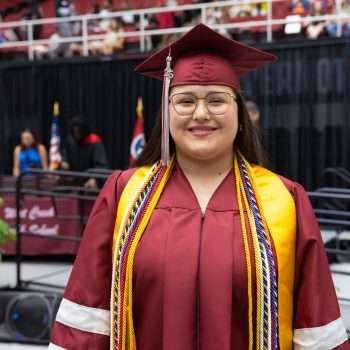 high school graduate wearing maroon gown and mortarboard smiling