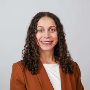 woman smiling in brown blazer in front of blank background