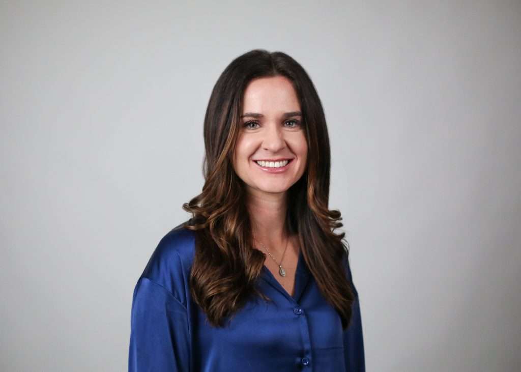 A headshot of a person with long brown hair wearing a blue shirt. 