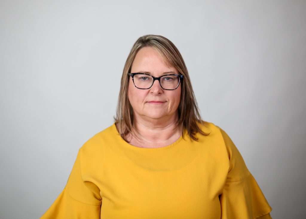 A headshot of a person with glasses wearing a yellow shirt. 