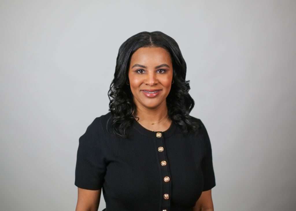 A headshot of a person with black hair wearing a black shirt with buttons. 
