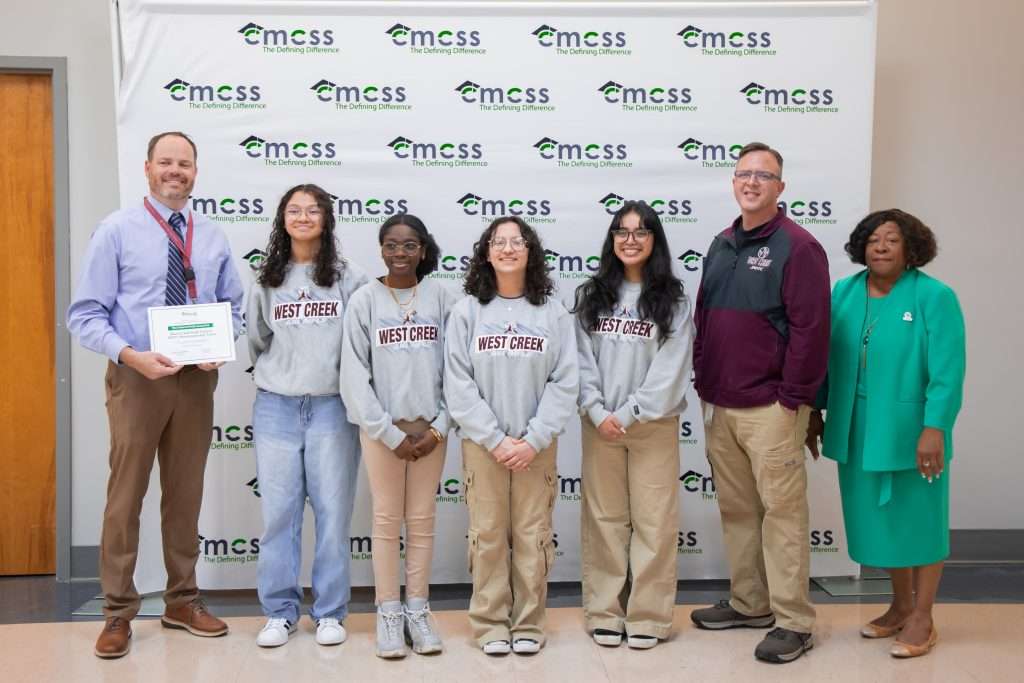 group of high school girls and male teachers in front of backdrop
