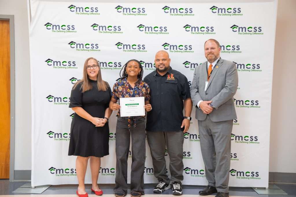 four people standing in front of a backdrop smiling with an award