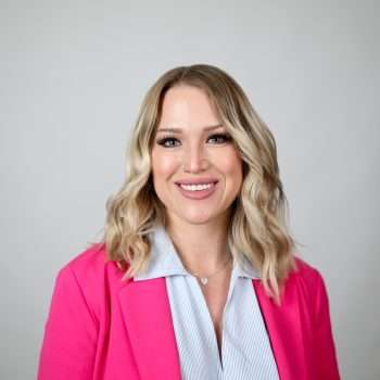 blonde woman in pink blazer smiling at camera