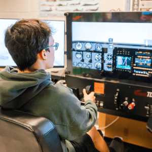 student wearing glasses in front of three computer screens with flight simulator