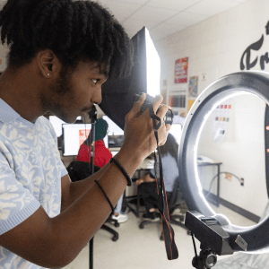 male student using a light ring to take a photo with a digital camera