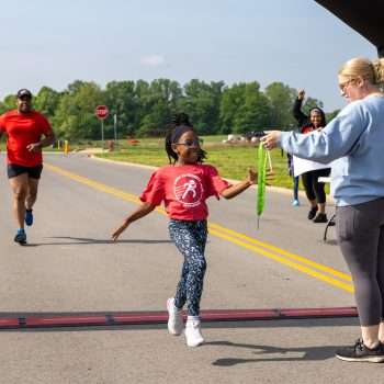 young girl receives a medal during a race from a woman standing at finish line