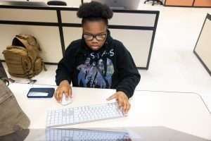high school student sits behind a desk looking at computer using a keyboard and mouse.