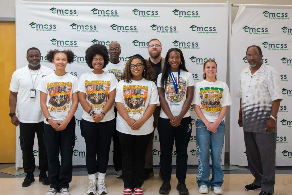 group of students in white shirts posing with adults in front of backdrop