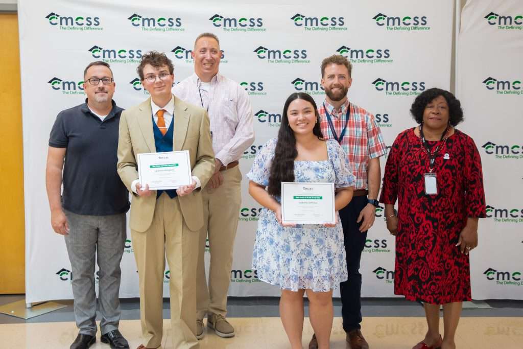 two students posing with adults in front of backdrop