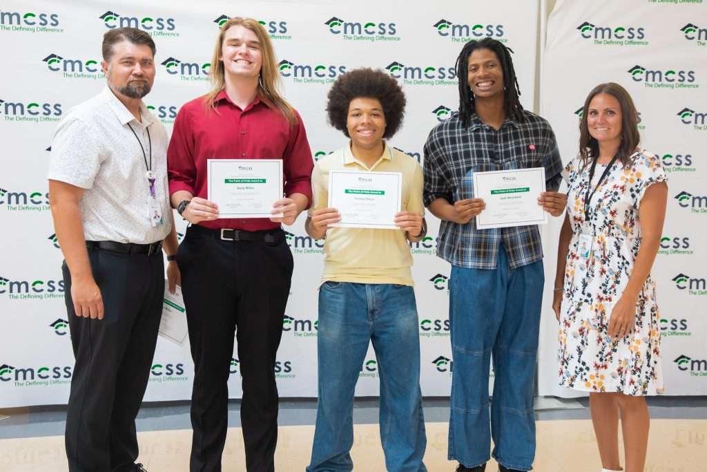 three students posing with adults in front of backdrop
