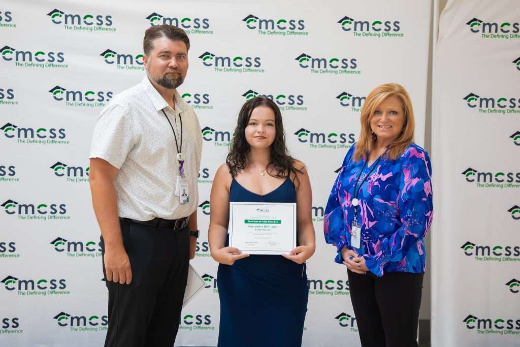 three people with an award in front of a backdrop