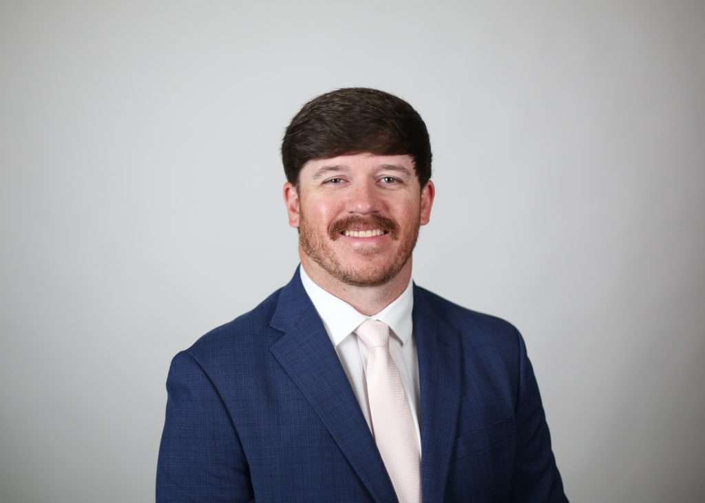 White man with a moustache wearing a blue blazer. 