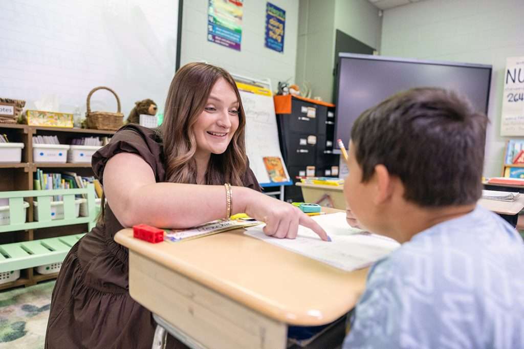 Teacher pointing at page and smiling at student.
