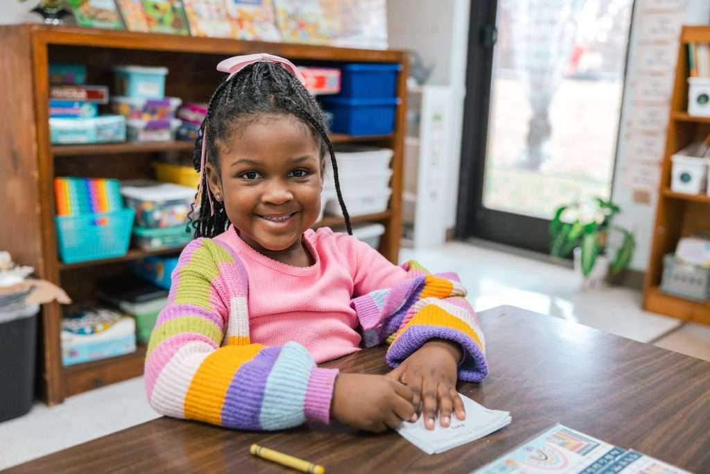 young girl sitting behind a desk hold a pencil smiling