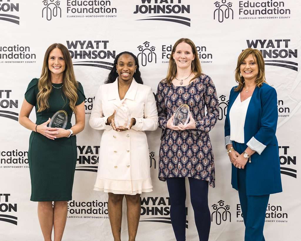 Group of women standing in front of a back drop holding awards