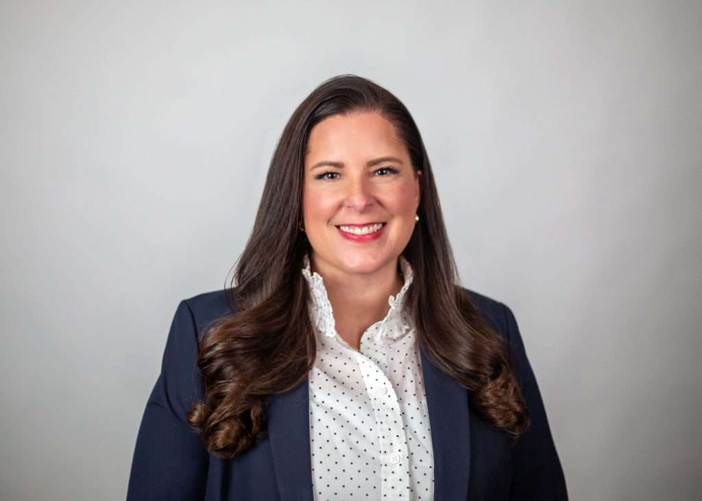 woman in white polka dot button up with blue blazer smiling at camera