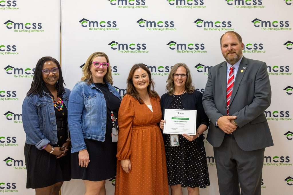 Five people standing in front of a backdrop that says CMCSS holding an award and smiling.