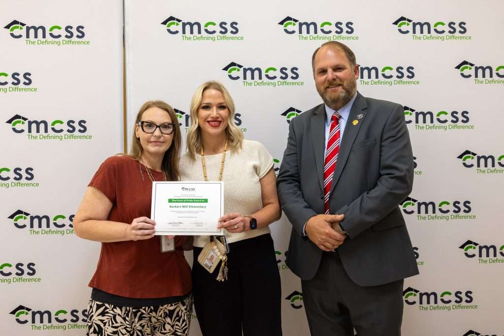 Three people standing in front of a backdrop that says CMCSS holding an award and smiling.