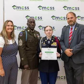 Four people standing in front of a backdrop that says CMCSS holding an award and smiling.