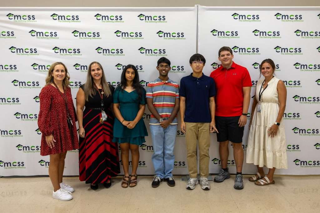 Seven people standing in front of a backdrop that says CMCSS holding an award and smiling.